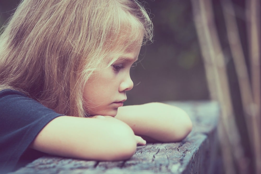 Portrait of sad blond little girl sitting on the bridge at the day time